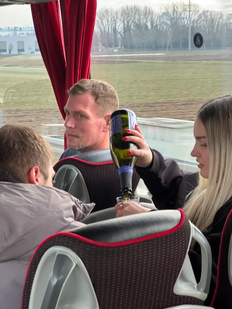 Drei Personen im Reisebus, eine hält eine grüne Glasflasche hoch
