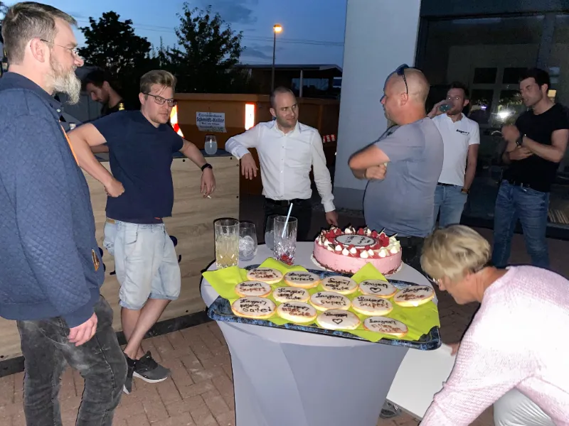 Kolleginnen und Kollegen abends um einen Stehtisch mit Torte und Gebäck
