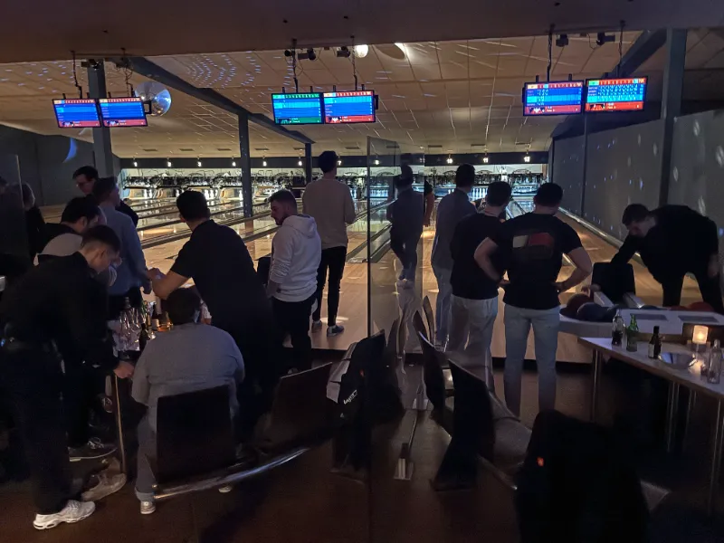 Größere Gruppe beim Bowling vor beleuchteten Bahnen und Anzeigemonitoren